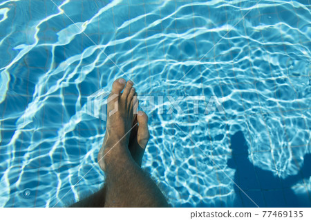 The feet of a young man in a swimming pool in summer, Spain. 77469135