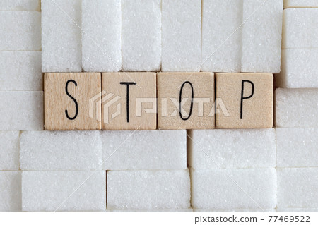Pile or wall of sugar cubes and stop word in block letters as advise on addiction calories excess and sweet unhealthy food abuse causing health problem and overweight background 77469522