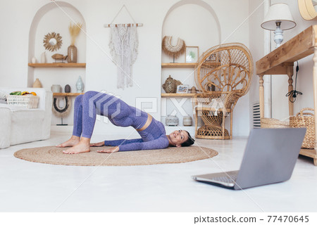 Fit woman trains at home and does exercise glute bridge 77470645