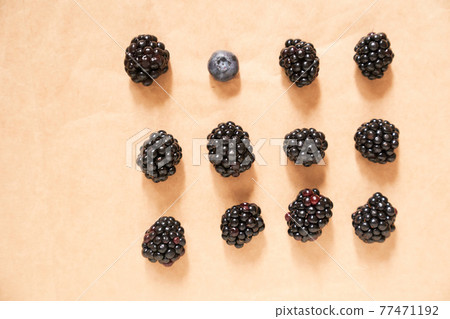 Eleven blackberries and one blueberry on a beige craft paper background 77471192