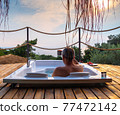 A handsome adult man lies in a hot tub at a luxurious exotic spa resort hotel balcony with sea and sunset view. 77472142