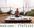 A man looking his smartphone in a hot tub at a luxurious exotic spa resort hotel balcony with sea and sunset view. 77472143