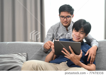 Happy of homosexual couple embracing and using digital tablet together in living room. Homosexual, LGBT concept. Happy of homosexual couple embracing and using digital tablet together in living room. Homosexual, LGBT concept. 77478338