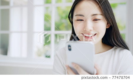A woman watching a smartphone with a smile A woman watching a smartphone with a smile 77478704