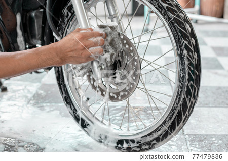 Washing a motorbike's wheels. 77479886
