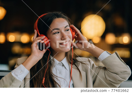 Young woman with headphones listen music while sitting in cafes Young woman with headphones listen music while sitting in cafes 77481662