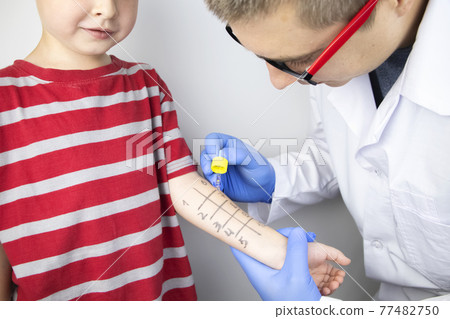 An allergist doctor makes a skin test for allergies. The boy is being examined in the laboratory, waiting for a reaction to allergens. An allergist doctor makes a skin test for allergies. The boy is being examined in the laboratory, waiting for a reaction to allergens. 77482750
