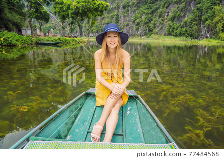 Woman tourist in boat on the lake Tam Coc, Ninh Binh, Viet nam. It's is UNESCO World Heritage Site, renowned for its boat cave tours. It's Halong Bay on land of Vietnam. Vietnam reopens borders after Woman tourist in boat on the lake Tam Coc, Ninh Binh, Viet nam. It's is UNESCO World Heritage Site, renowned for its boat cave tours. It's Halong Bay on land of Vietnam. Vietnam reopens borders after 77484568
