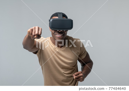 Cheerful man in VR glasses waving his fists Cheerful man in VR glasses waving his fists 77484640