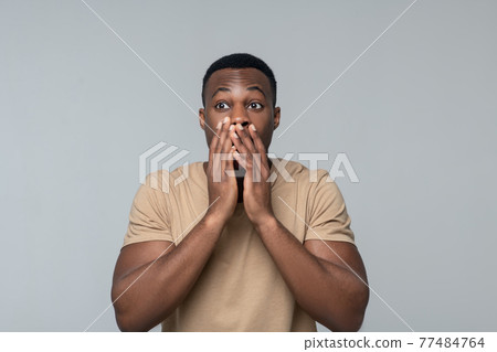 Amazed dark skinned man touching mouth with hands Amazed dark skinned man touching mouth with hands 77484764