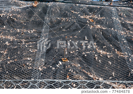 Strengthening the mountain slope with a metal mesh that prevents rockfall on the road. Abstract background of the security concept. Strengthening the mountain slope with a metal mesh that prevents rockfall on the road. Abstract background of the security concept. 77484878