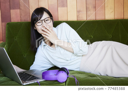 一個女人坐在沙發上看她電腦上的視頻 一個女人坐在沙發上看她電腦上的視頻 77485388