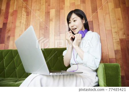 A woman sitting on the sofa watching a video on her computer 77485421