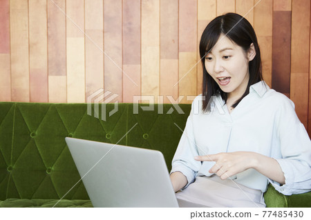 A woman sitting on the sofa watching a video on her computer 77485430