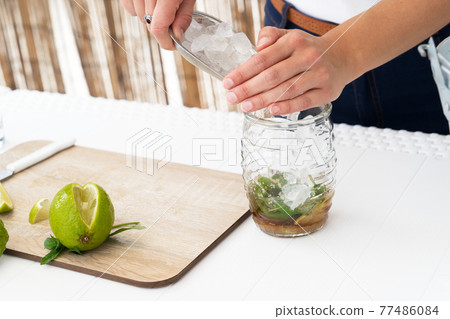 Bartender putting ice cube into shaker while making fresh cocktail with lime juice Bartender putting ice cube into shaker while making fresh cocktail with lime juice 77486084
