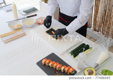 Male chef in uniform peeling avocado for sushi Male chef in uniform peeling avocado for sushi 77486085