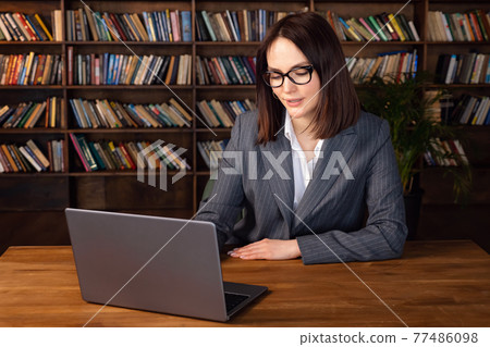 Woman in formal suit working on laptop while sitting at the table 77486098
