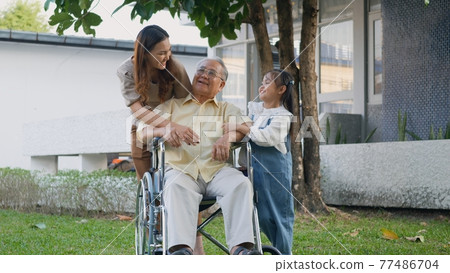 Disabled senior grandpa on wheelchair with grandchild and mother in park Disabled senior grandpa on wheelchair with grandchild and mother in park 77486704