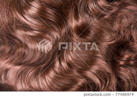 Brown hair texture. Wavy long curly light brown hair close up as background. Hair extensions, materials and cosmetics, hair care. Hairstyle, haircut or dying in salon. 77486974