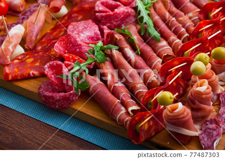 Slicing sausages and ham with cherry tomatoes and olives on board 77487303