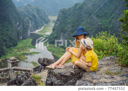 Mother and son tourists on the lake Tam Coc and pagoda of Hang Mua temple, Ninh Binh, Viet nam. It's is UNESCO World Heritage Site, renowned for its boat cave tours. It's Halong Bay on land of Vietnam 77487332