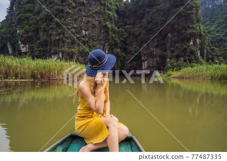 Woman tourist in boat on the lake Tam Coc, Ninh Binh, Viet nam. It's is UNESCO World Heritage Site, renowned for its boat cave tours. It's Halong Bay on land of Vietnam. Vietnam reopens borders after Woman tourist in boat on the lake Tam Coc, Ninh Binh, Viet nam. It's is UNESCO World Heritage Site, renowned for its boat cave tours. It's Halong Bay on land of Vietnam. Vietnam reopens borders after 77487335