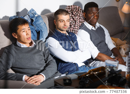 Three sad friends are watching football and cheering together Three sad friends are watching football and cheering together 77487336