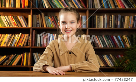 Schoolgirl model poses sitting at new brown wooden desk Schoolgirl model poses sitting at new brown wooden desk 77488247