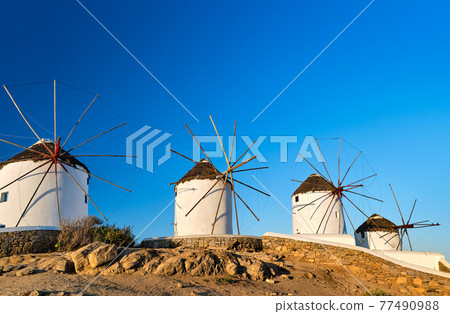 Famous tourist attraction of Mykonos, Cyclades, Greece. Four traditional whitewashed windmills by waterfront. Summer, travel destination, iconic view. 77490988