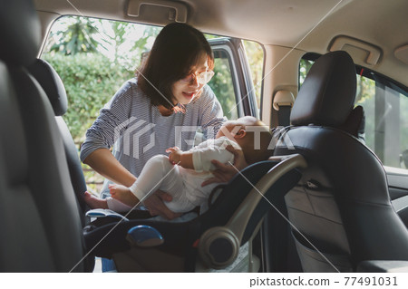 Asian young mother putting her baby son into car seat Asian young mother putting her baby son into car seat 77491031