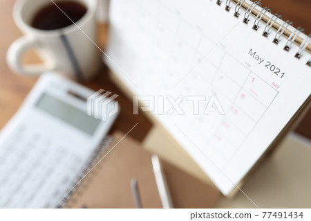 Loose-leaf paper calendar standing on table near calculator and cup of coffee closeup 77491434