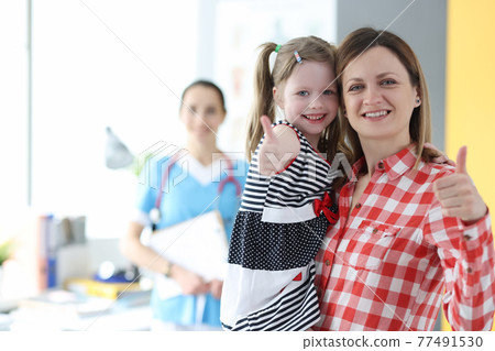 Mother holding little girl in her arms and showing ok gesture at doctor appointment 77491530