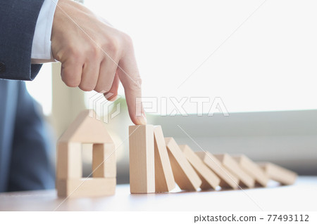 Male hand stopping falling wooden blocks in front of toy house closeup Male hand stopping falling wooden blocks in front of toy house closeup 77493112