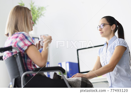 Disabled woman in wheelchair is drinking tea and talking with psychologist Disabled woman in wheelchair is drinking tea and talking with psychologist 77493120