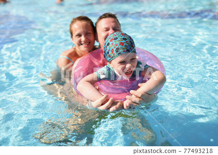 Little girl with circle and parents swimming in pool Little girl with circle and parents swimming in pool 77493218
