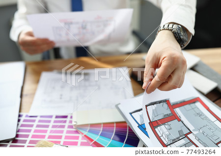Man designer sitting at table and holding design project of apartment in his hands Man designer sitting at table and holding design project of apartment in his hands 77493264
