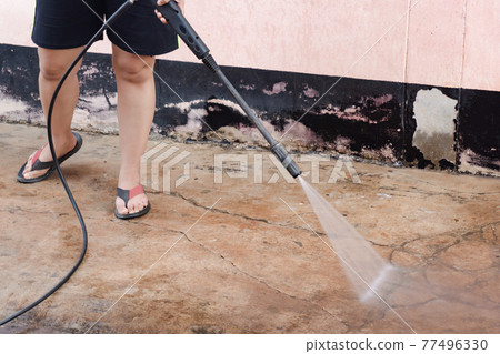 Worker cleaning dirty floor with high pressure washer. 77496330