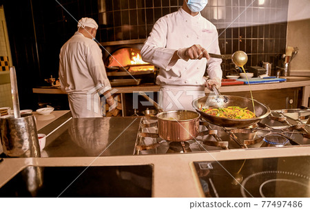 Chef adding sauce to vegetables in cooking pan 77497486