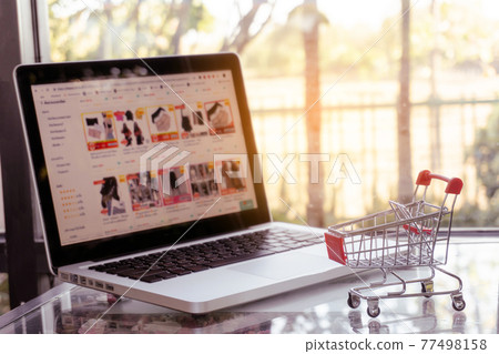 Online shopping concept - shopping cart or trolley and laptop on table 77498158