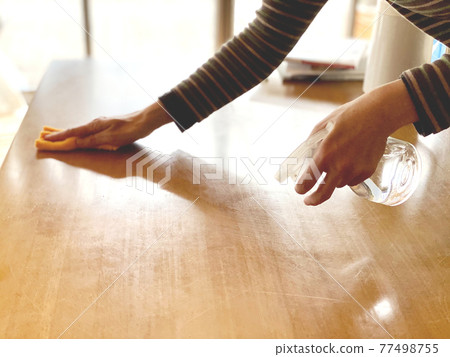 Housewife's hand wiping the table with a disinfectant spray 77498755