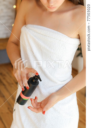 Beautiful fresh young woman applying cream or body wash on hand from dispenser indoors Beautiful fresh young woman applying cream or body wash on hand from dispenser indoors 77503020