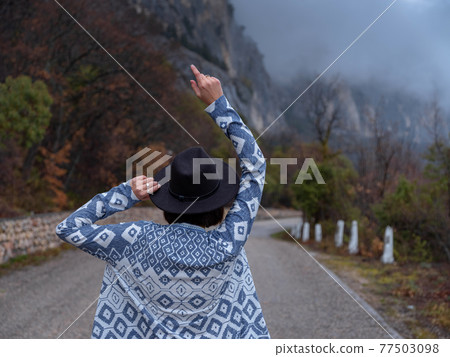 Stylish hipster woman in a hat walking down a mountain road 77503098