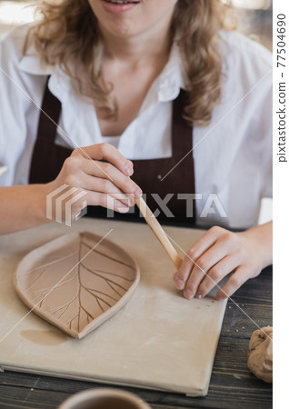Young woman curving clay product edges Pottery workshop. 77504690