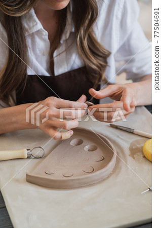 Artisan female potter prepares material for her pottery. Woman hands attach clay part to future ceramic product. Work close-up. 77504691