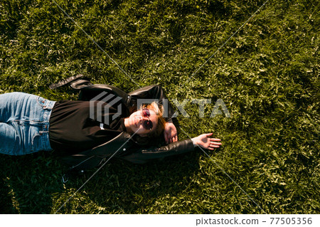 Beautiful healthy Young Woman lying and relaxing on the green grass 77505356