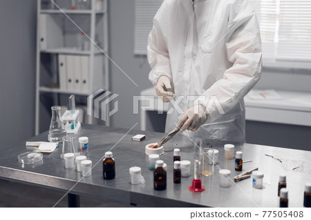 A scientist working in a chemical laboratory. Laboratory equipment and glassware containing chemical liquids in the foreground A scientist working in a chemical laboratory. Laboratory equipment and glassware containing chemical liquids in the foreground 77505408