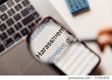 "harassment" word on phone's screen and magnifying glass close-up 77505976
