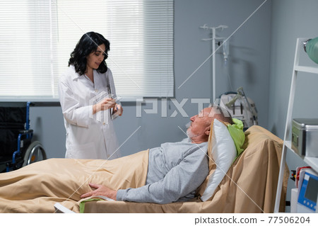 A female doctor talking to her patient, who is lying in bed in a hospital ward A female doctor talking to her patient, who is lying in bed in a hospital ward 77506204