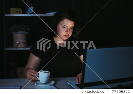 Night work. Woman drinking coffee working late Night work. Woman drinking coffee working late 77506892