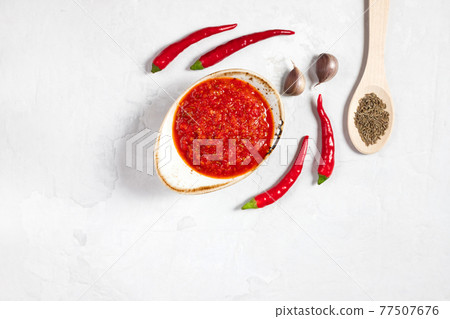 Hot chili pepper sauce paste harissa. Adjika on a white background. Traditional Tunisia, Georgian and Arabic cuisine. Homemade rose harissa in a bowl. Hot chili pepper sauce paste harissa. Adjika on a white background. Traditional Tunisia, Georgian and Arabic cuisine. Homemade rose harissa in a bowl. 77507676